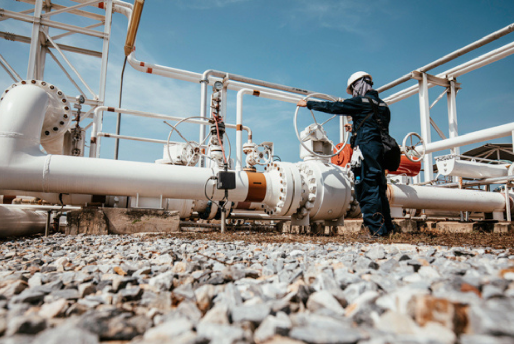 Person wearing safety equipment inspecting industrial piping and valve systems.