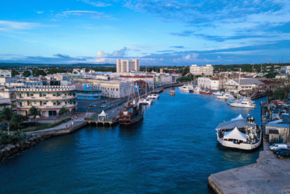 Aerial view of a Barbados waterfront city with boats docked along a canal and buildings lining the shoreline.