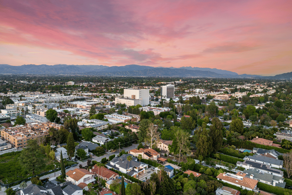 Aerial view of Orange County neighborhoods and commercial buildings with mountains in the distance at sunset