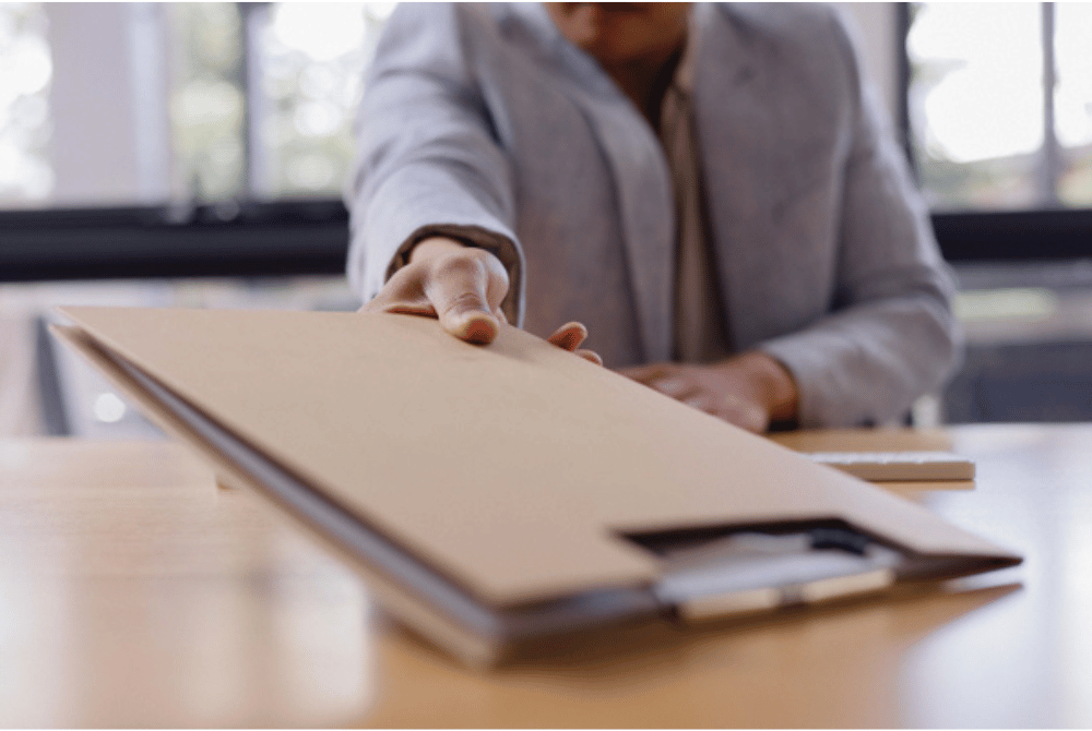 Person handing over a document folder on a desk