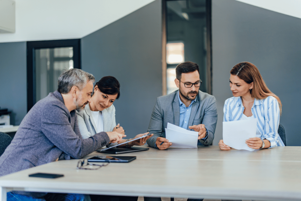 Four colleagues reviewing documents together at a conference table in a modern office.