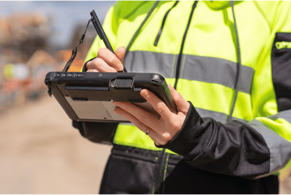 Person in a high-visibility safety jacket using a stylus to enter information on a handheld tablet device